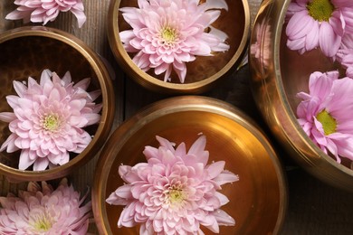 Photo of Tibetan singing bowls with water and beautiful flowers on wooden table, flat lay