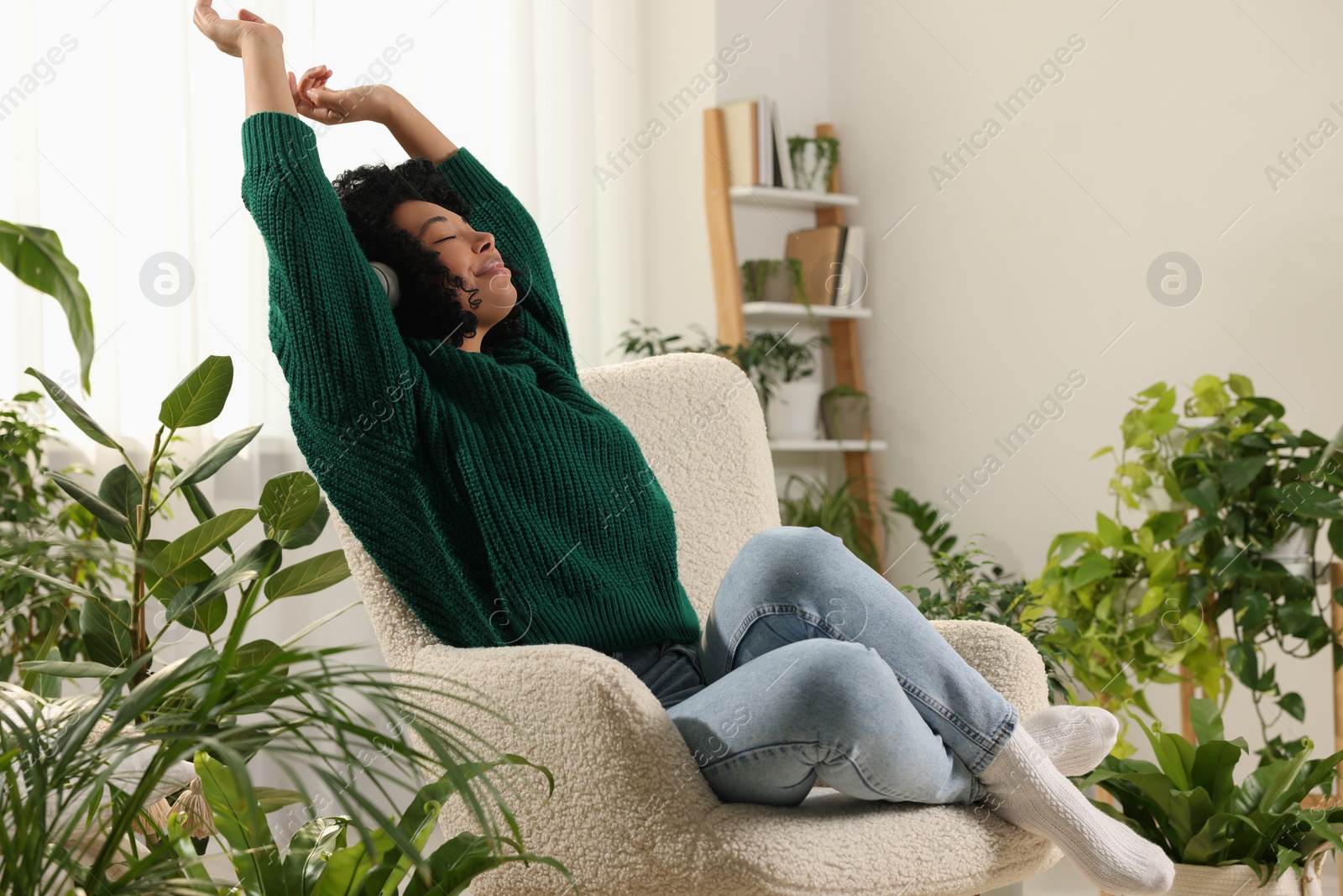 Photo of Woman wearing headphones and listening music in room with beautiful houseplants