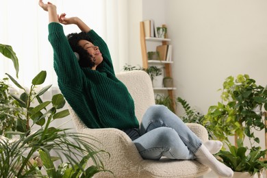 Woman wearing headphones and listening music in room with beautiful houseplants