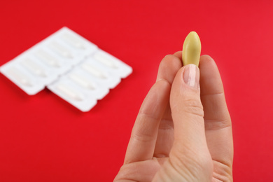 Photo of Woman holding suppository on red background, closeup. Hemorrhoid treatment