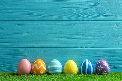 Painted Easter eggs on green grass against wooden background, space for text