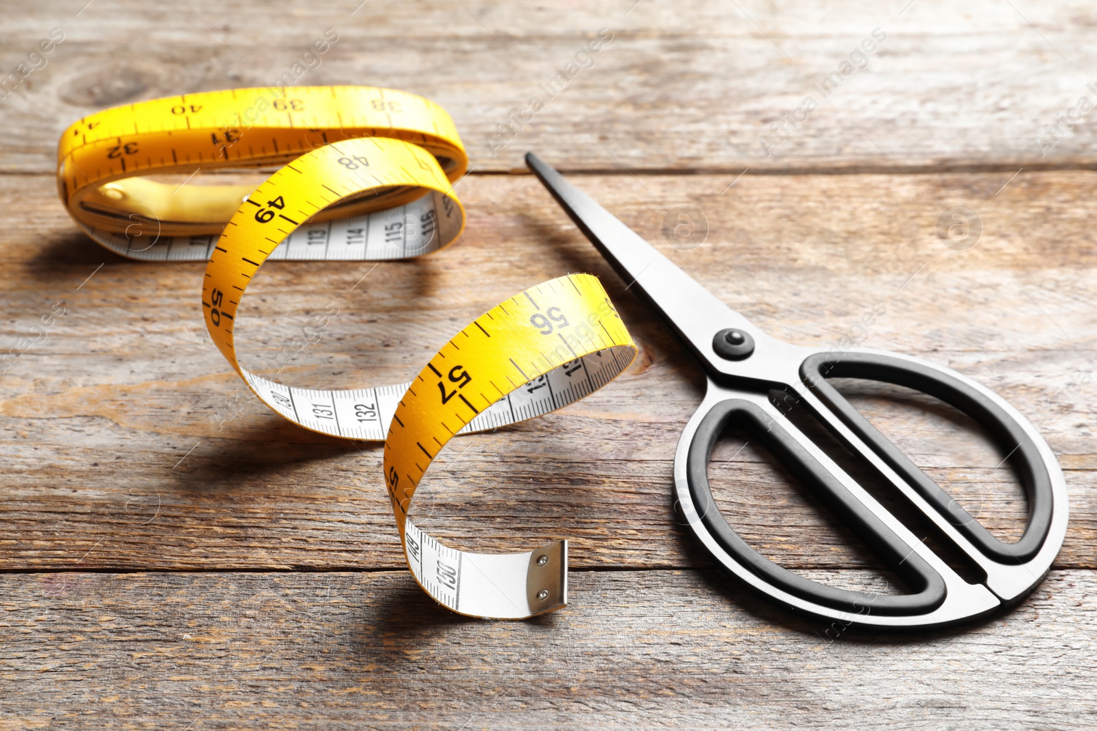 Photo of Scissors and measuring tape on wooden background. Tailoring equipment