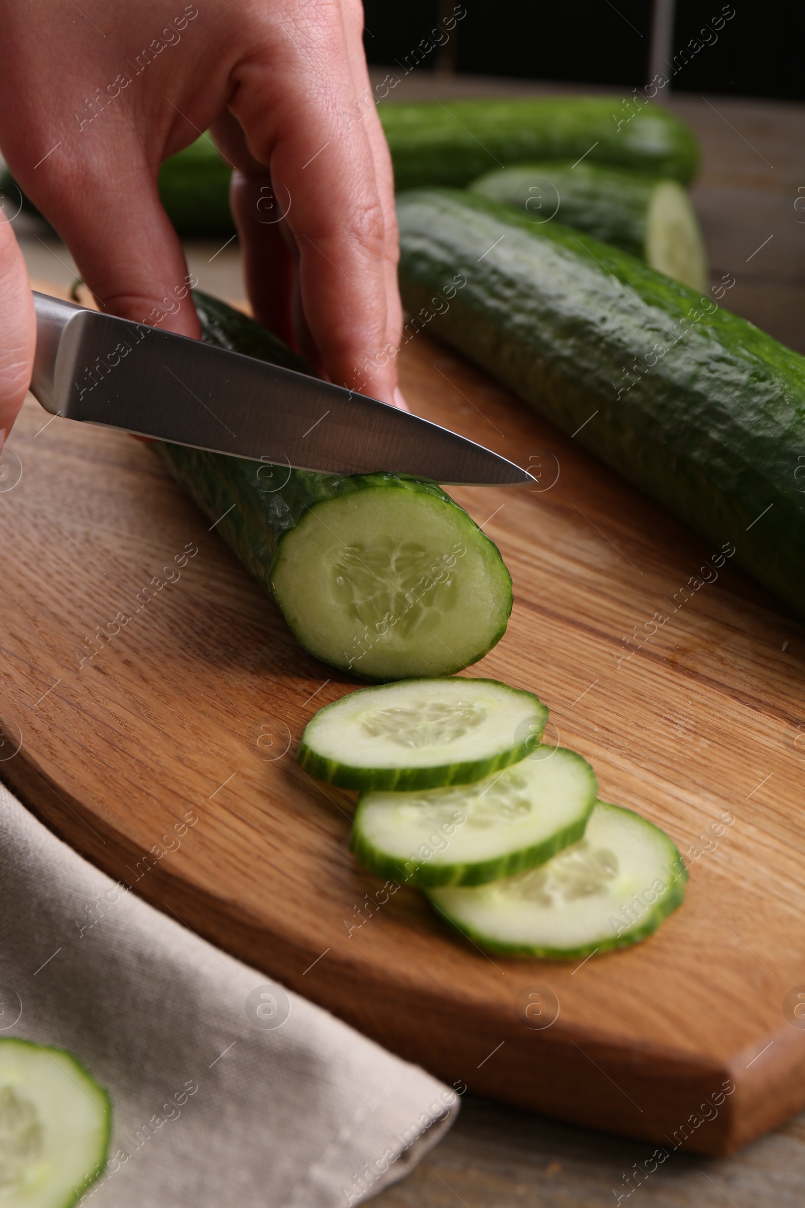 Photo of Woman cutting cucumber on wooden board at table, closeup