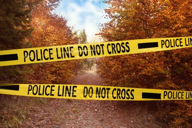 Image of Yellow police tape isolating crime scene. Restricted area of autumn park 