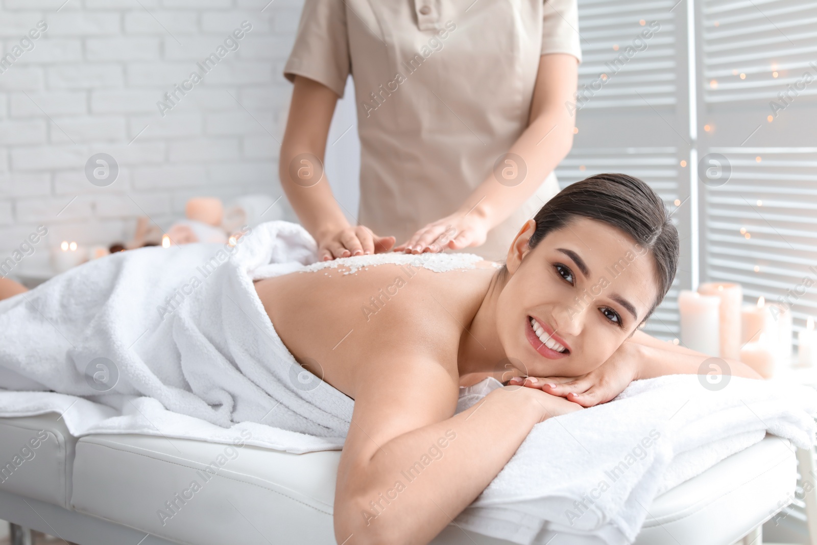 Photo of Young woman having body scrubbing procedure with sea salt in spa salon