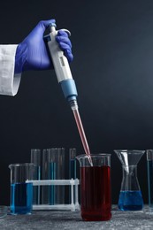 Photo of Laboratory analysis. Scientist dripping sample with micropipette into beaker at grey table, closeup