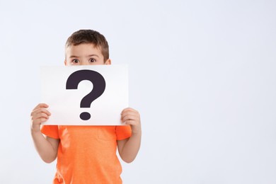 Photo of Emotional little boy holding paper with question mark on white background