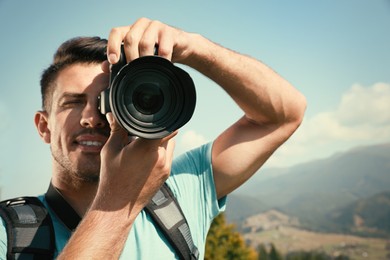 Photo of Professional photographer taking picture with modern camera in mountains, focus on lens