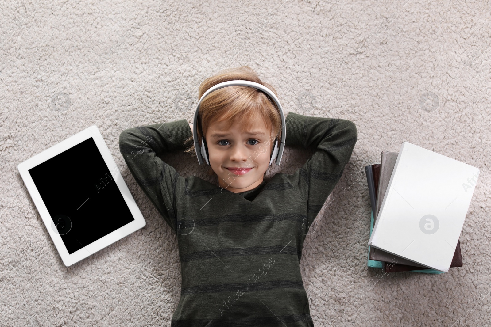 Photo of Cute little boy with headphones and tablet listening to audiobook on floor indoors, flat lay