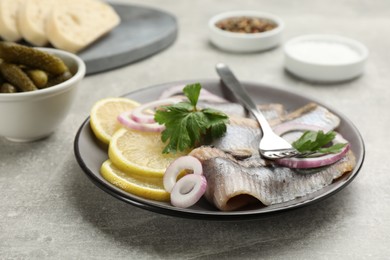 Photo of Delicious salted herring fillets served with lemon, onion rings and parsley on grey table, closeup