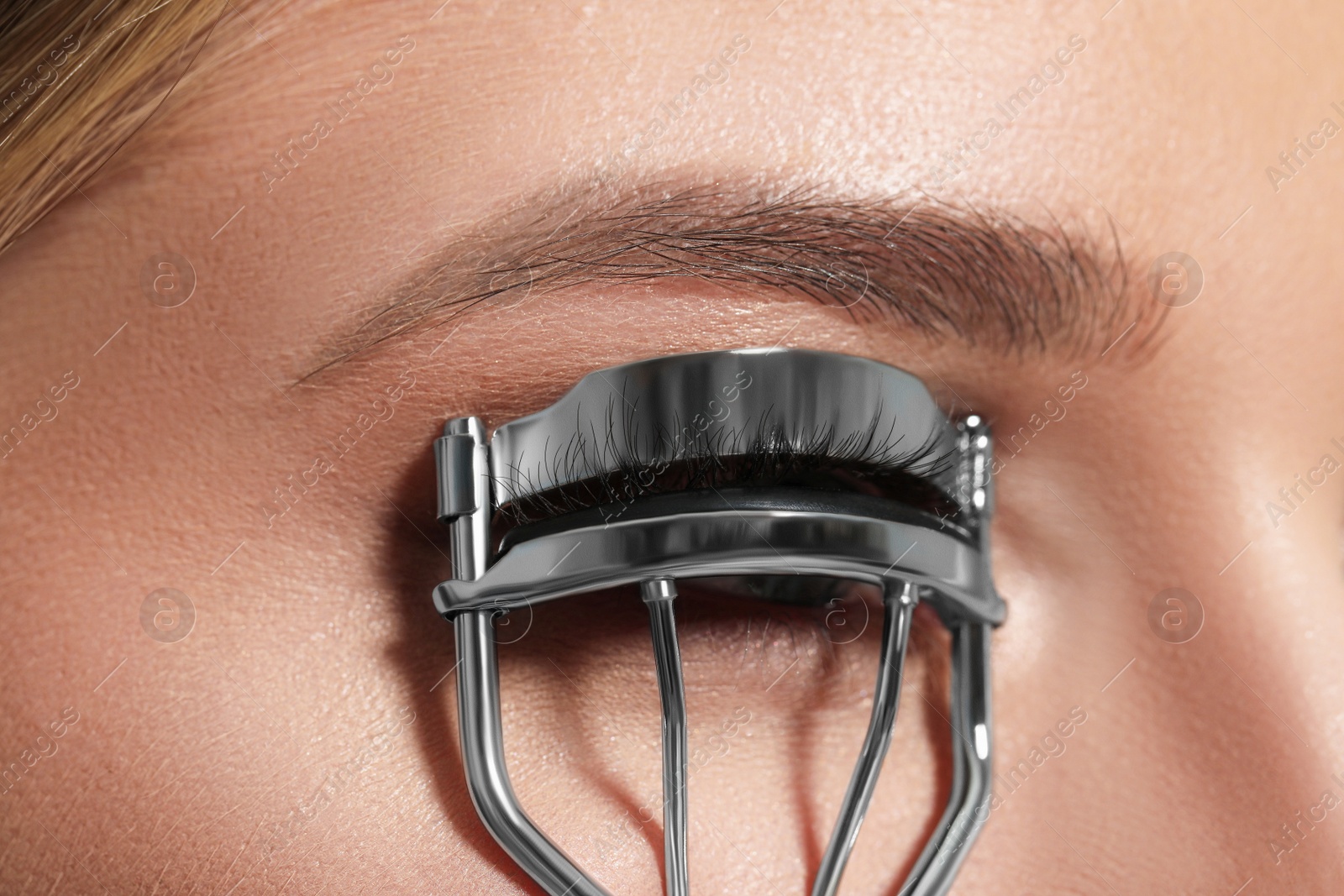 Photo of Young woman using eyelash curler, closeup view