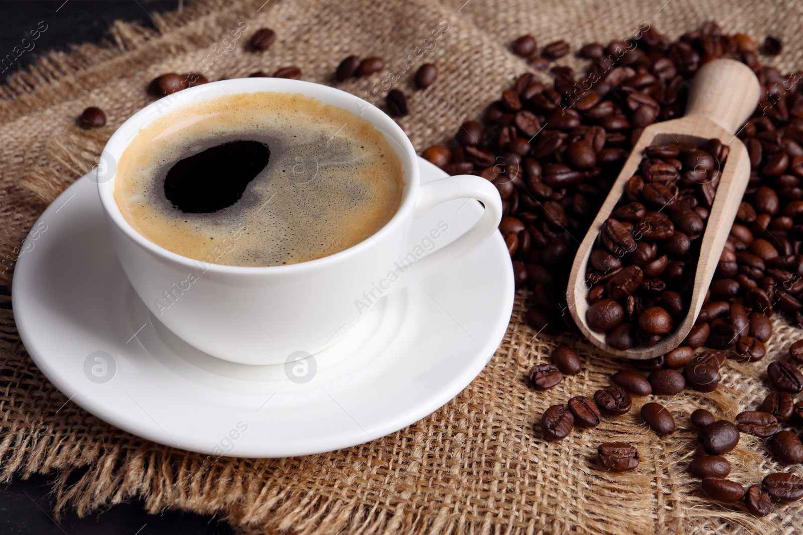 Photo of Cup of hot aromatic coffee and scoop with roasted beans on sackcloth