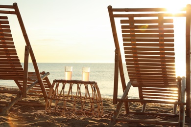 Wooden deck chairs and wicker table with cocktails on sandy beach. Summer vacation