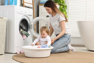 Photo of Mother with her daughter washing baby clothes in bathroom