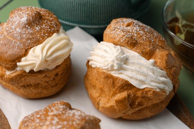 Photo of Delicious profiteroles filled with cream and tea on green background, closeup