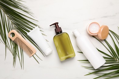 Photo of Shampoo bottles, wooden comb, hair and face mask and palm leaves on white marble table, flat lay