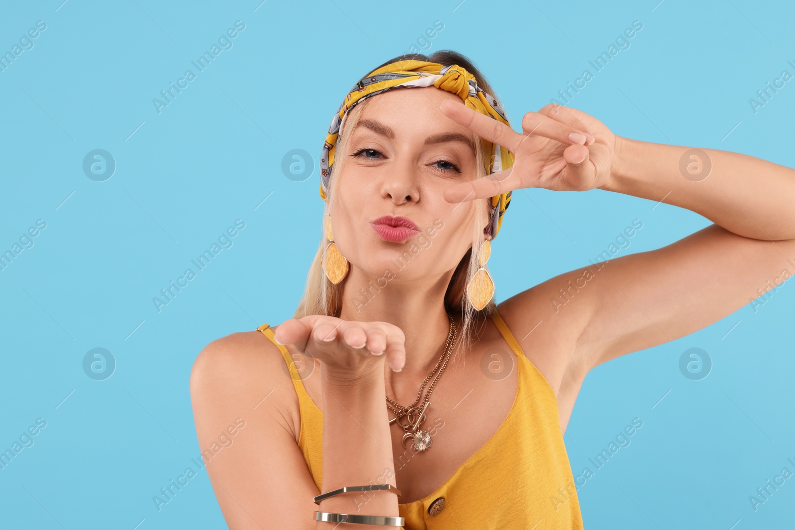 Photo of Portrait of hippie woman showing peace sign and blowing kiss on light blue background