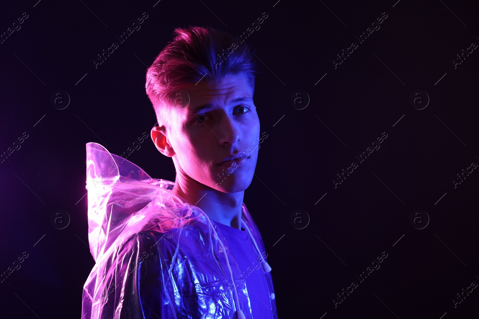 Photo of Young man wearing clear coat on dark background in neon lights. Space for text