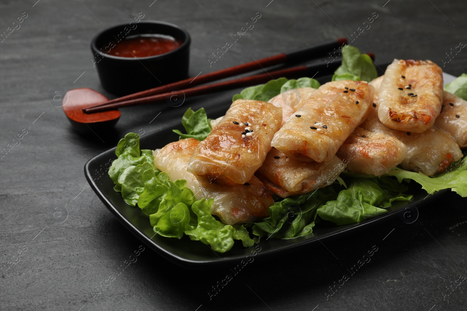 Photo of Tasty fried spring rolls, lettuce and sauce on black table, closeup