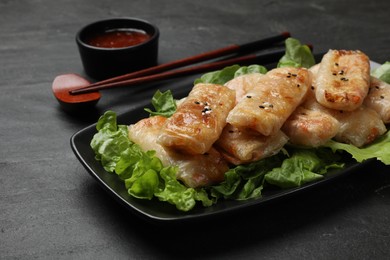 Photo of Tasty fried spring rolls, lettuce and sauce on black table, closeup