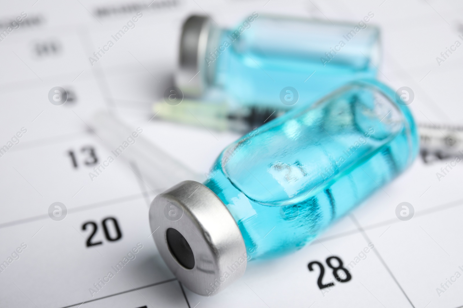 Photo of Vial and syringe on calendar, closeup. Vaccination and immunization