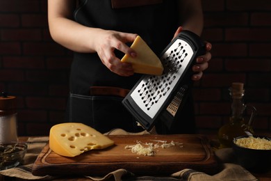 Photo of Woman grating cheese at wooden table, closeup