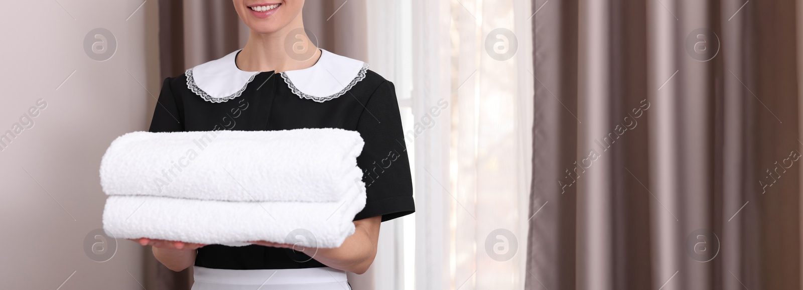 Image of Beautiful chambermaid with stack of fresh towels in hotel room, closeup view with space for text. Banner design