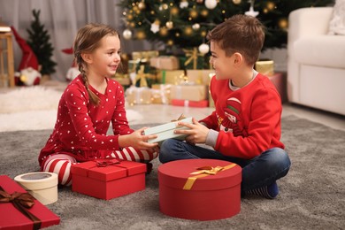 Cute little children with gift box near Christmas tree at home