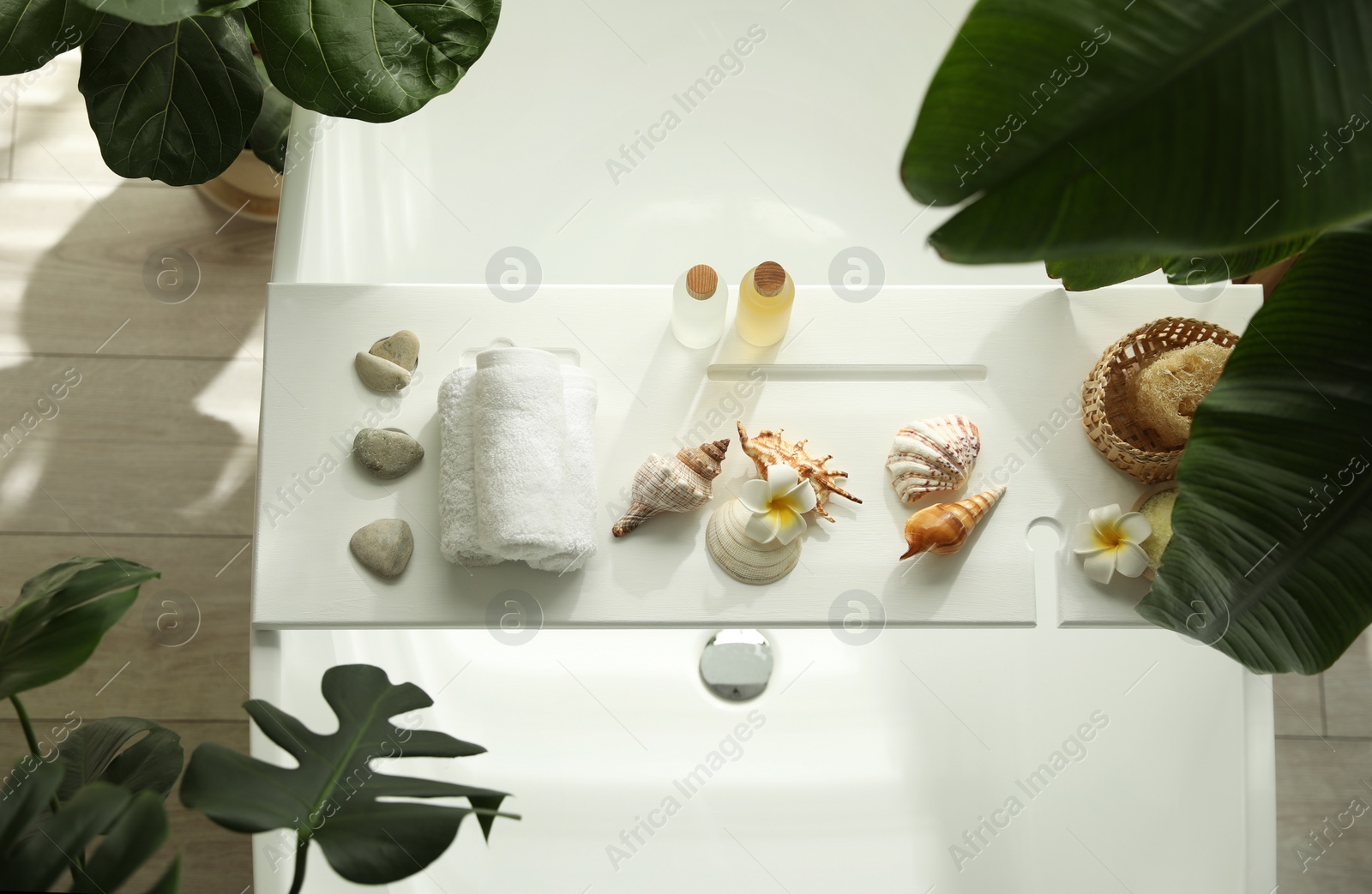Photo of Bath tray with spa products, towels and shells on tub in bathroom, top view