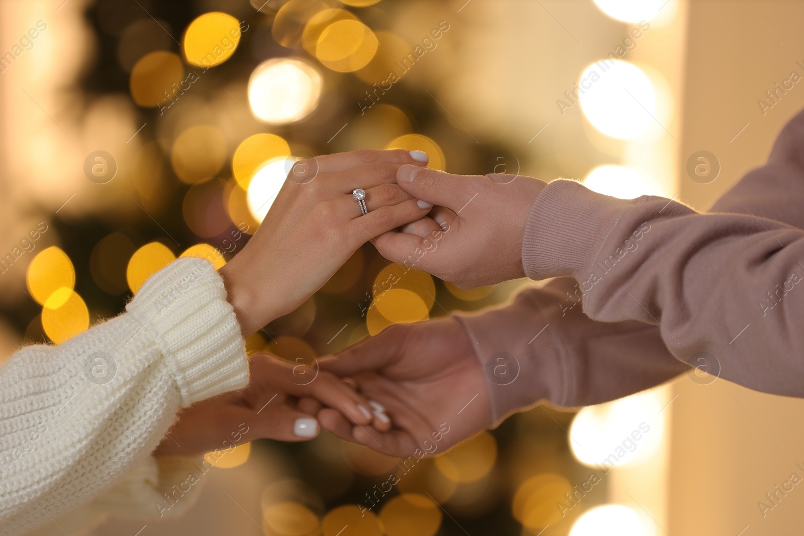 Photo of Making proposal. Woman with engagement ring and her fiance holding hands against blurred lights, closeup