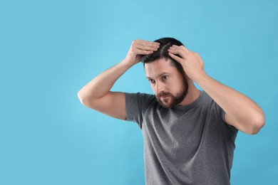 Photo of Handsome man examining his hair and scalp on light blue background. Space for text