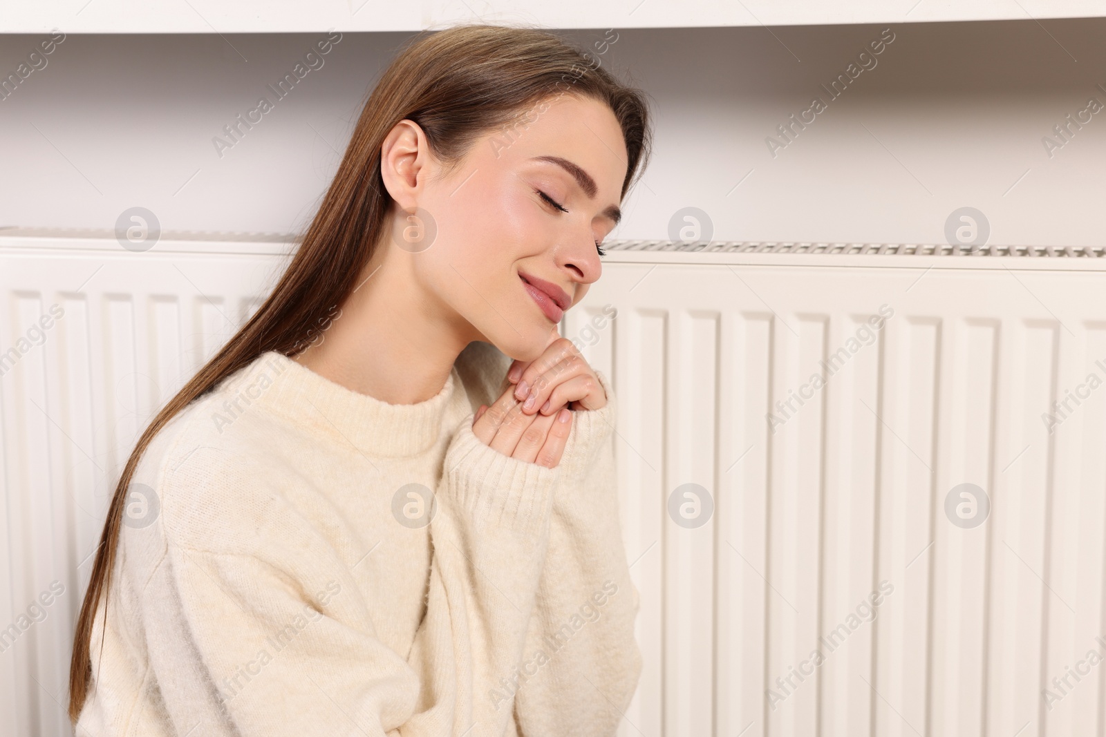 Photo of Young woman warming near heating radiator, space for text