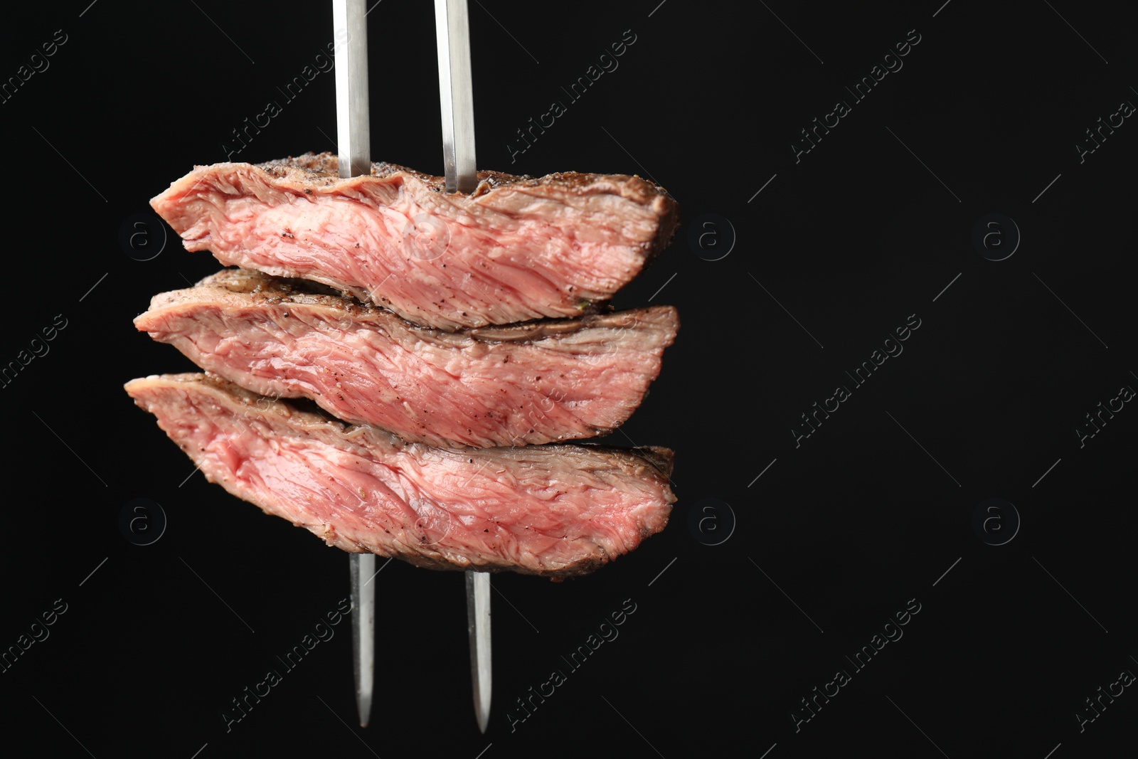 Photo of Meat fork with grilled beef pieces on black background, closeup. Space for text