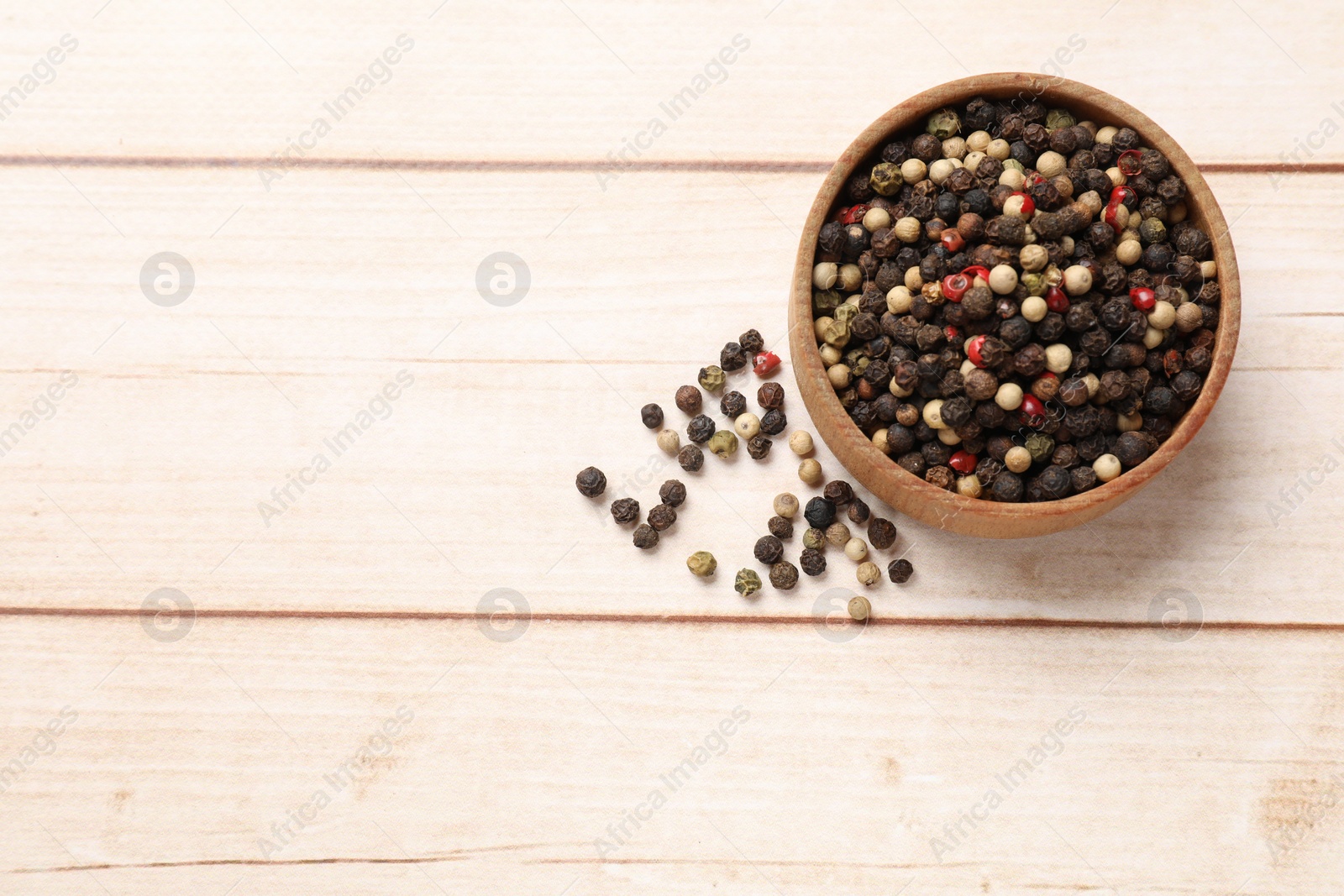 Photo of Aromatic spices. Different peppers in bowl on wooden table, top view and space for text