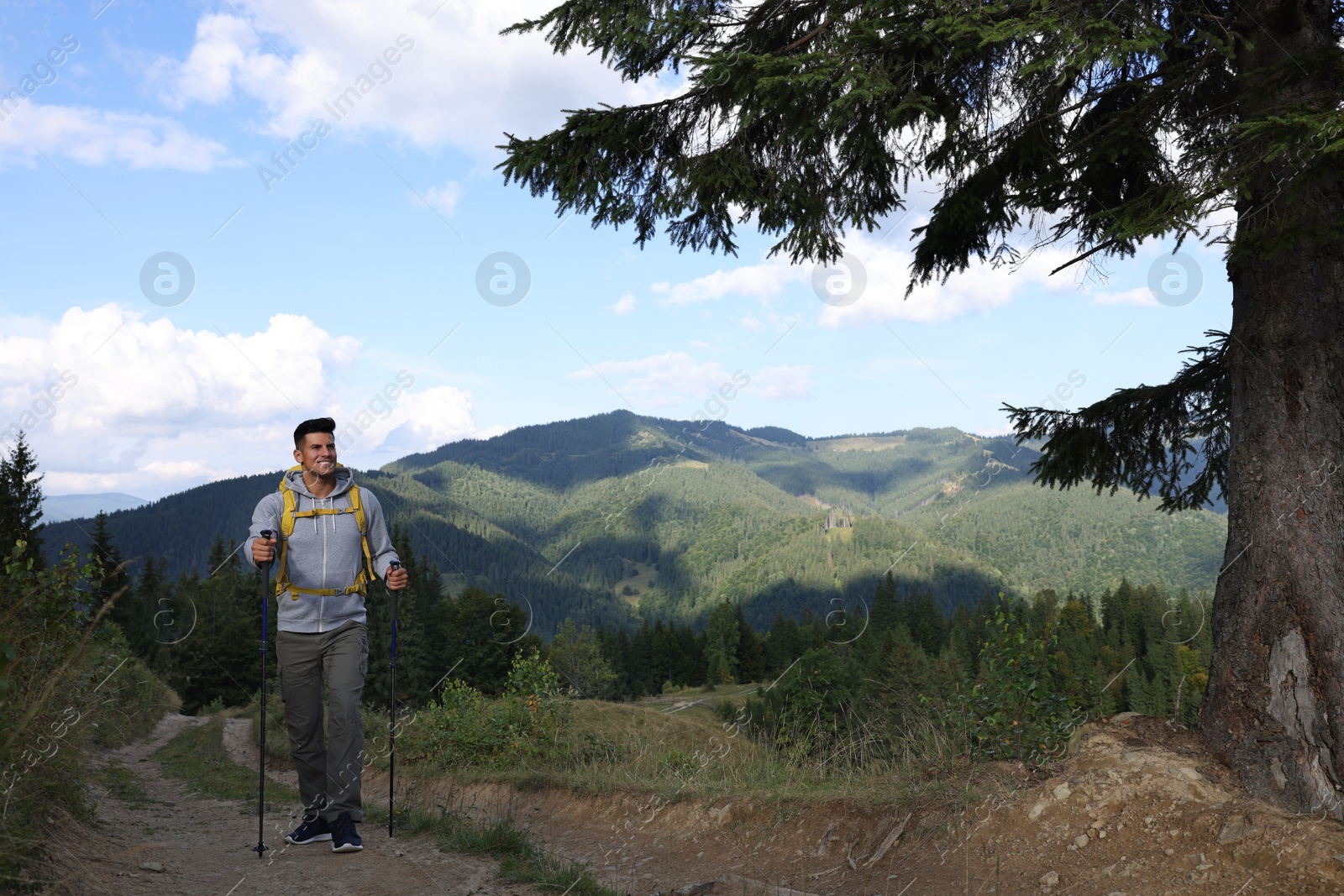 Photo of Tourist with backpack and trekking poles hiking through mountains, space for text