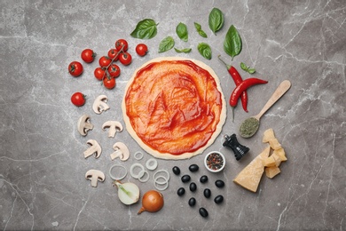 Dough with sauce and ingredients for pizza on table, top view