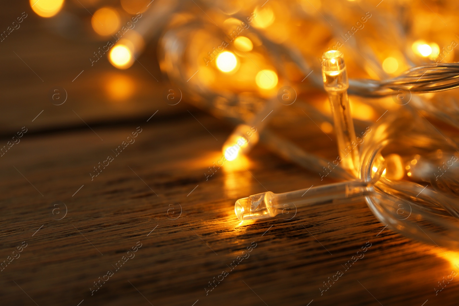 Photo of Glowing Christmas lights on wooden table, closeup view