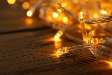 Glowing Christmas lights on wooden table, closeup view