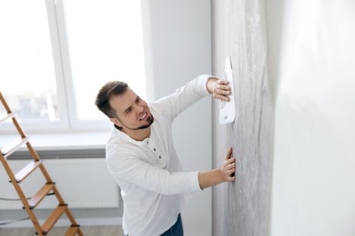 Man smoothing stylish gray wallpaper in room