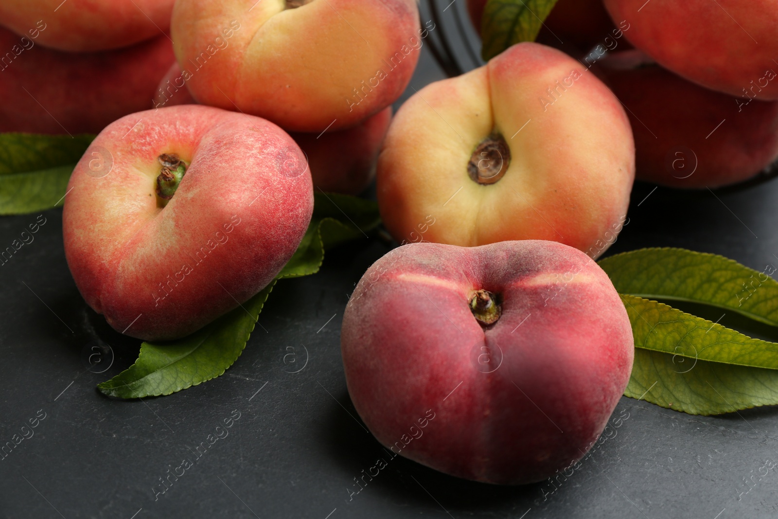 Photo of Fresh ripe donut peaches with leaves on dark table, closeup