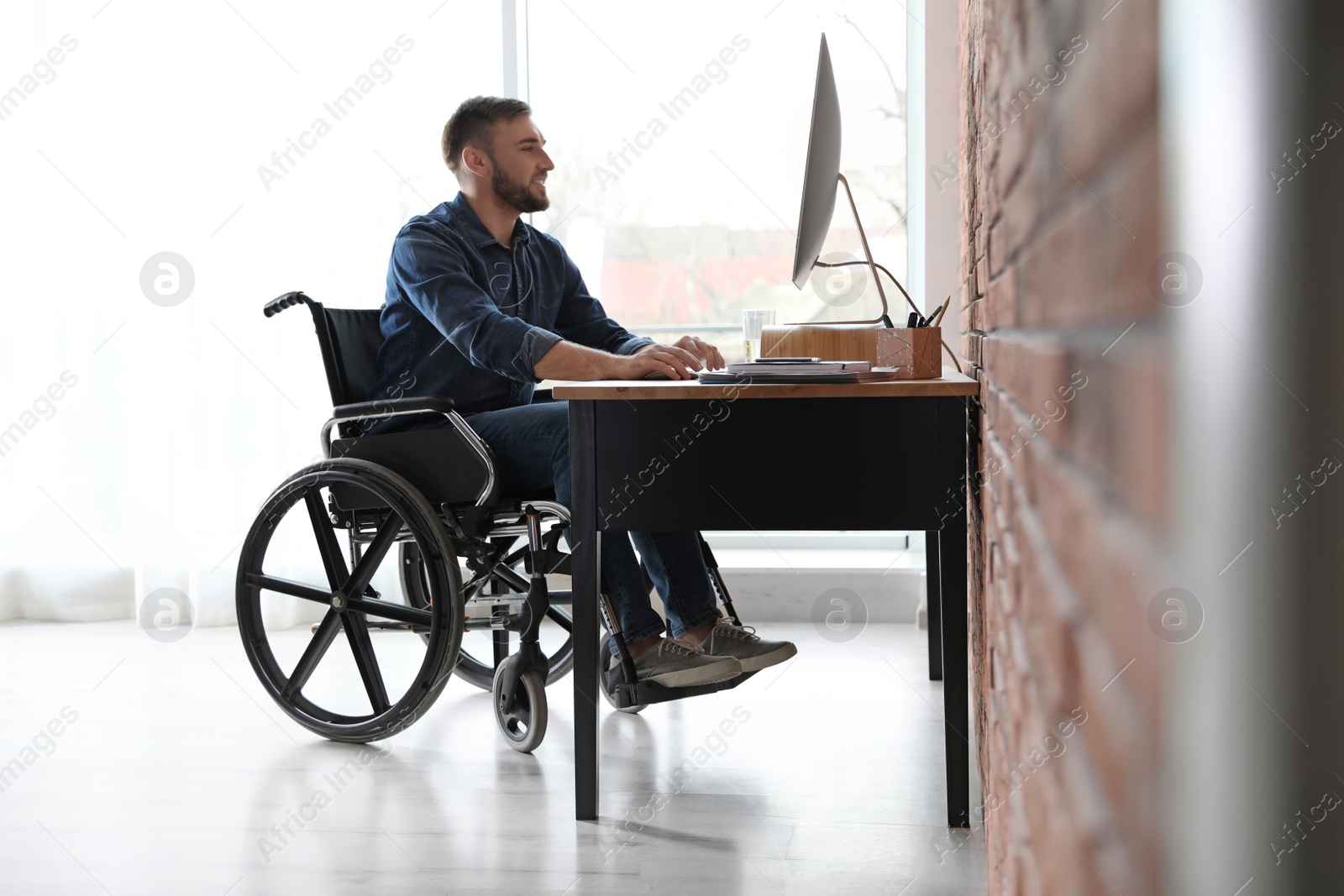 Photo of Man in wheelchair working with computer at table indoors
