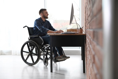Man in wheelchair working with computer at table indoors