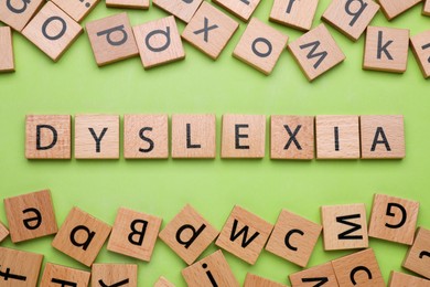 Wooden cubes with word Dyslexia on light green background, flat lay