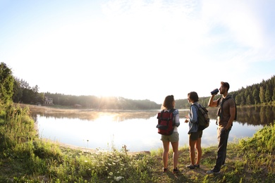 Young friends on shore of beautiful lake, wide-angle lens effect. Camping season