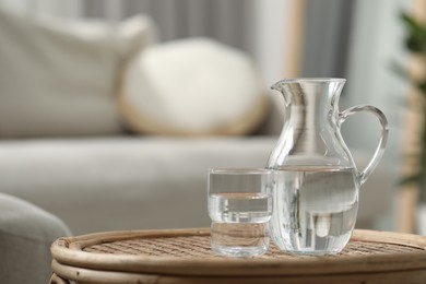 Jug and glass with clear water on wicker surface against blurred background, closeup. Space for text