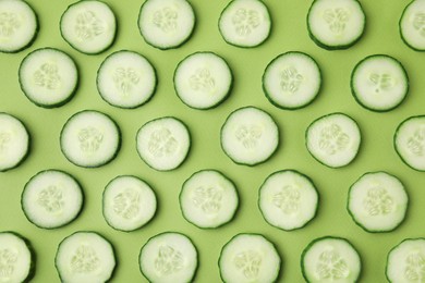 Photo of Fresh slices of cucumbers on green background, top view