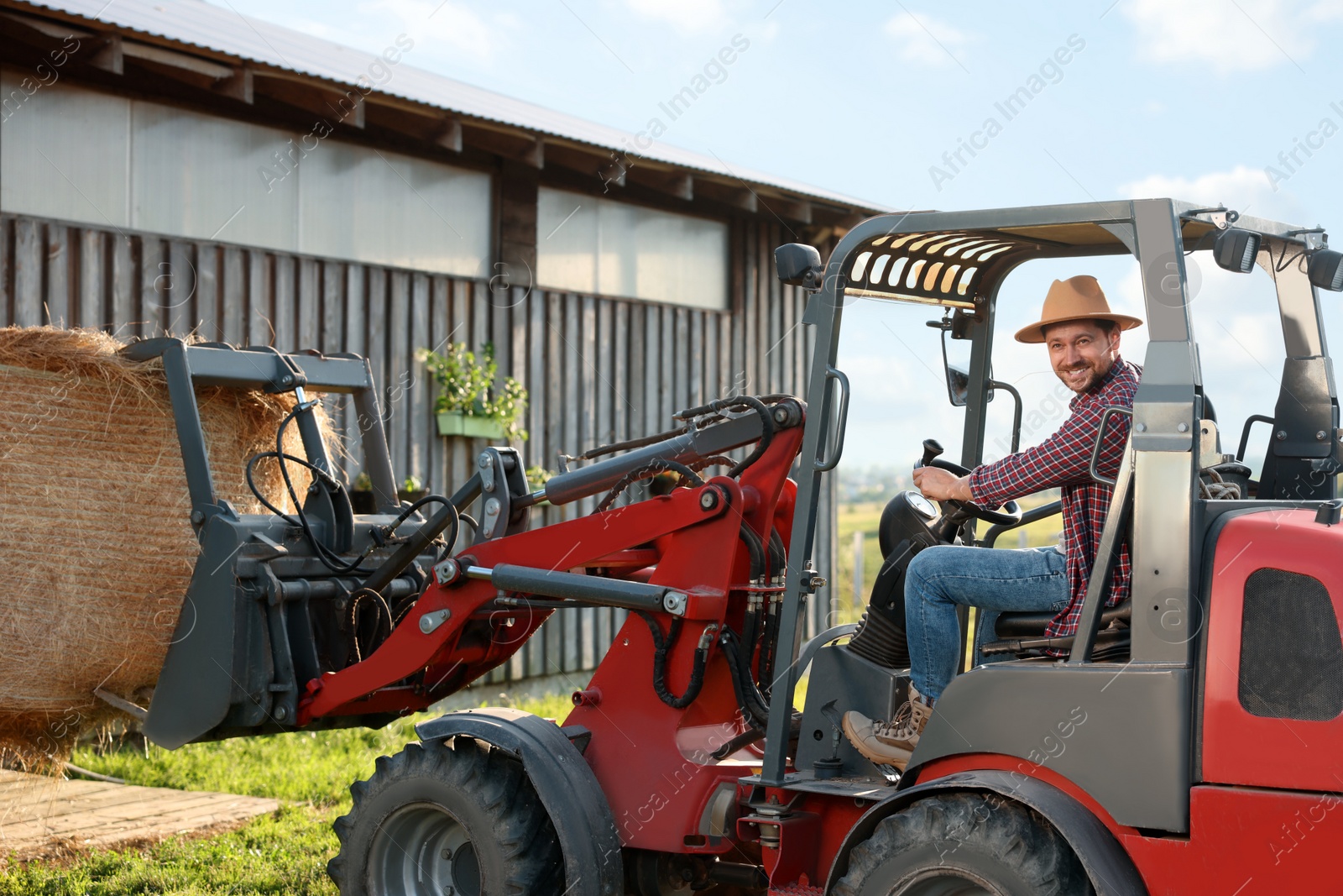 Photo of Farmer in loader transporting hay on farm. Agriculture equipment