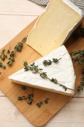 Board with pieces of tasty camembert cheese and thyme on light wooden table, top view