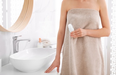 Young woman with roll on deodorant in bathroom, closeup view. Space for text