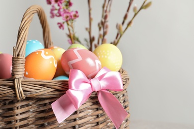 Wicker basket with painted Easter eggs and flowers on color background, closeup